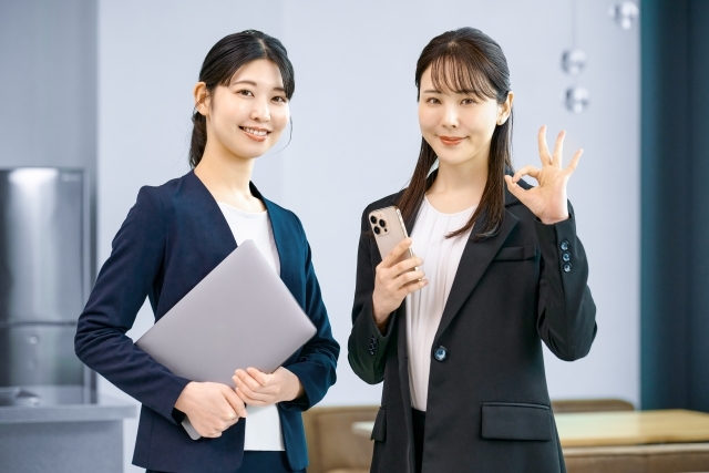 ノートパソコンとスマートフォンを持ち笑顔の女性