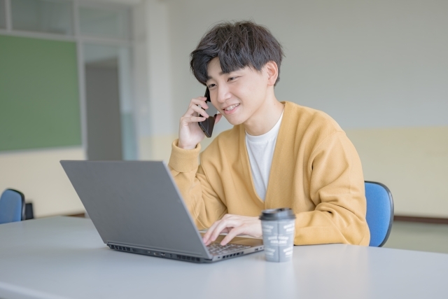 パソコンで作業をしながら電話をする男性